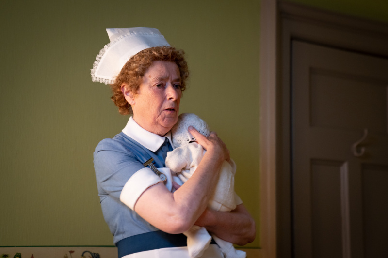  Linda Basset como la enfermera Phyllis Crane sosteniendo a un bebé