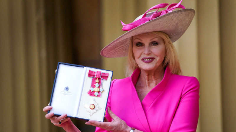   Joanna Lumley em uma roupa rosa brilhante posando com seu prêmio DBE em 2022