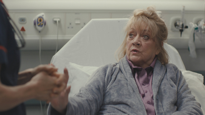   Amanda Barrie อยู่บนเตียงในบทผู้ป่วยอุบัติเหตุ Elsie