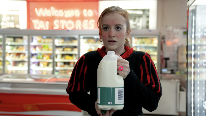   Máiréad Tyers con un top rosso e nero mentre Jen in Extraordinary tiene in mano un cartone di latte in un supermercato.