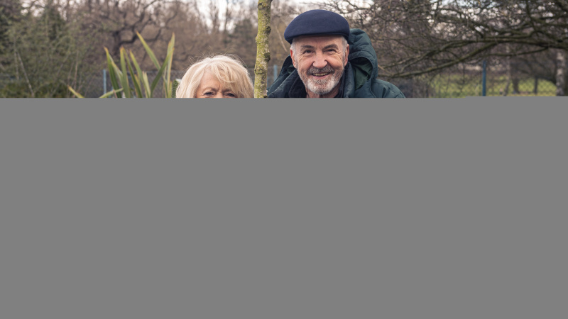   Alison & Larry: Billericay'dan Barry'ye filminde açık mavi paltolu Alison Steadman elinde bir ağaç tutuyor ve koyu renk şapka ve ceketle Larry Lamb'in yanında duruyor.