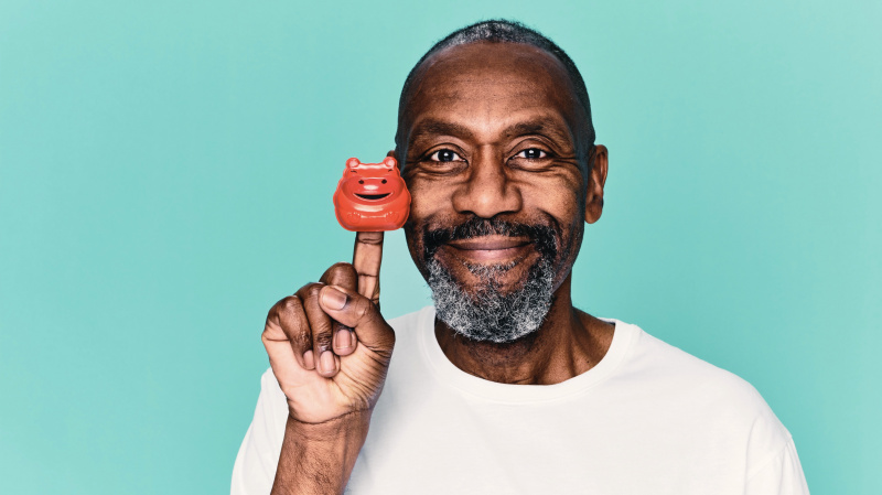   Sir Lenny Henry v bielom tričku drží červený nos na prste na modrom pozadí pre Comic Relief.