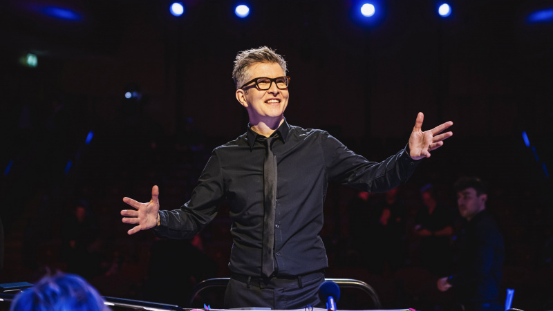   Gareth Malone într-o cămașă neagră și cravată conduce un cor în Gareth Malone's Easter Passion.