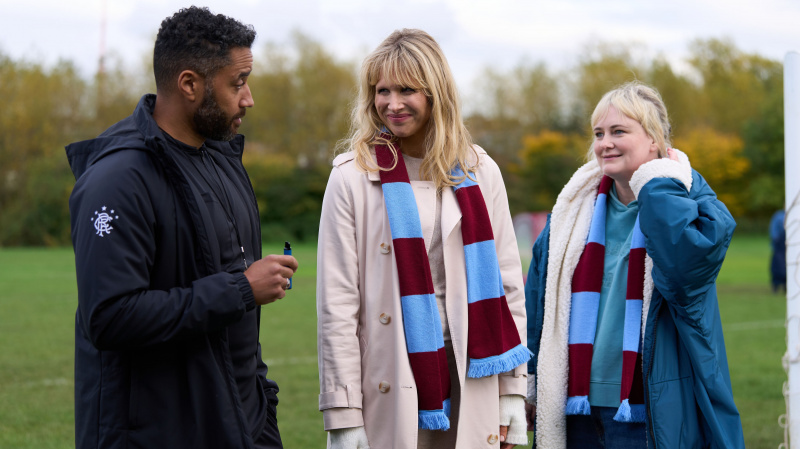  Samuel Anderson v čiernej bunde, keď Mal stojí na poli s Lucy Punch, ako Amanda a Philippa Dunne ako Anne v Claret aj Blue Scarves v Amandalande.