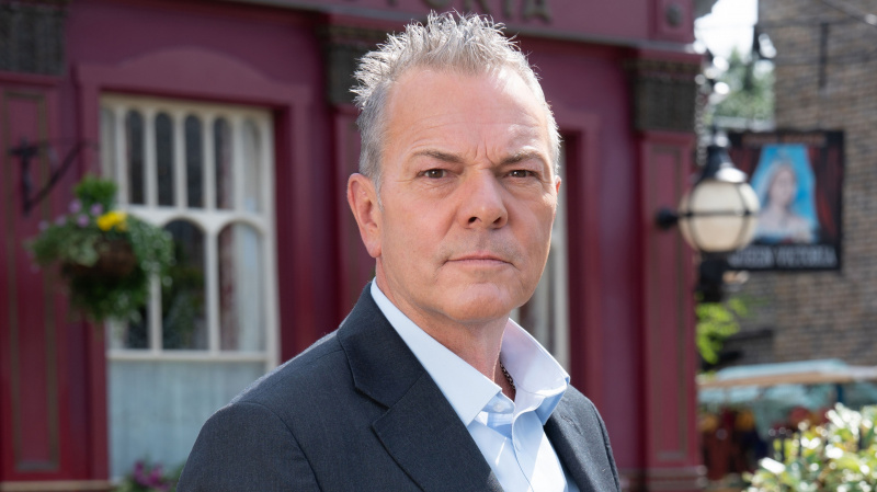  Michael French ca David Wicks în EastEnders purtând un costum și stând în fața pubului
