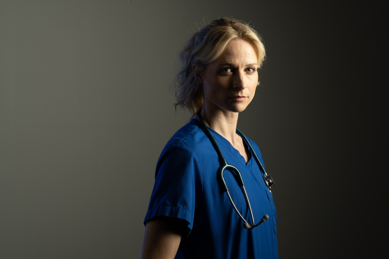 นักแสดงทุจริต: Niamh Algar เป็น Dr. Lucinda Edwards สวมหูฟังแพทย์และสครับสีน้ำเงิน