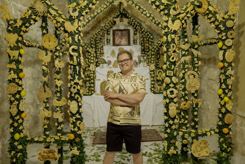  Alan stojí v Salemi's bread museum, in front of a shrine to various local specialty breads, and surrounded by wall decorations consisting of breads in the shape of animals and flowers