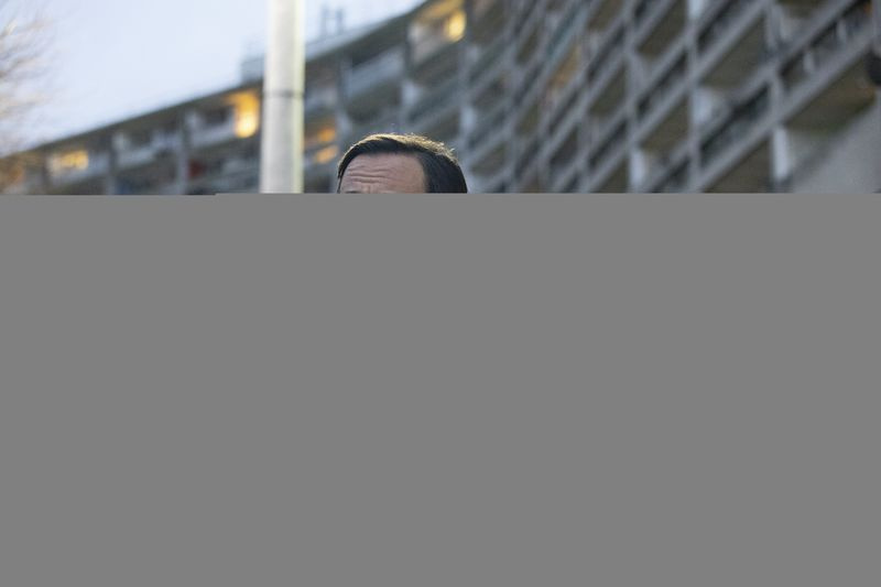 Kenny (Emun Elliott) se naslanja na odprta vrata avtomobila pred velikim stanovanjskim blokom