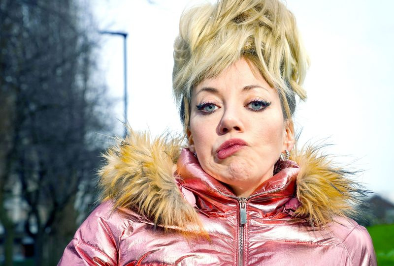 Diane Morgan dans le rôle de Mandy, avec une haute coiffure blonde, une expression pincée et une veste matelassée rose