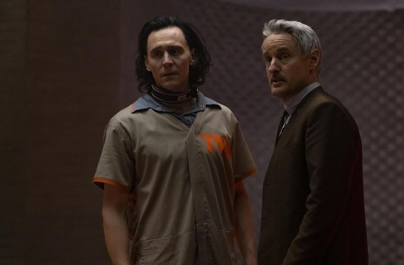 Ένας αιχμάλωτος και με γιακά Loki (Tom Hiddleston) φοράει ένα μπεζ πουκάμισο TVA ενώ λαμβάνει οδηγίες από τον Μόμπιους M Mobius (Owen Wilson)