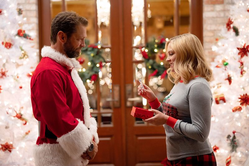ジェイソン・プリーストリーとメリッサ・ジョーン・ハートがクリスマスっぽいドアの前に立ち、プレゼントを交換します