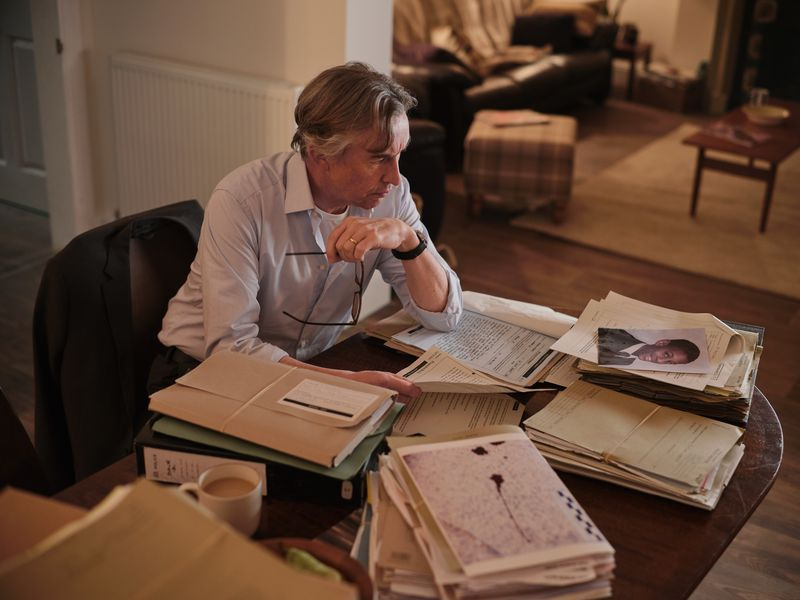 Stephen: DCI Clive Driscoll (Steve Coogan) siedzi przy swoim stole w domu, otoczony oryginalnymi aktami sprawy ze śledztwa w sprawie morderstwa Stephena Lawrence